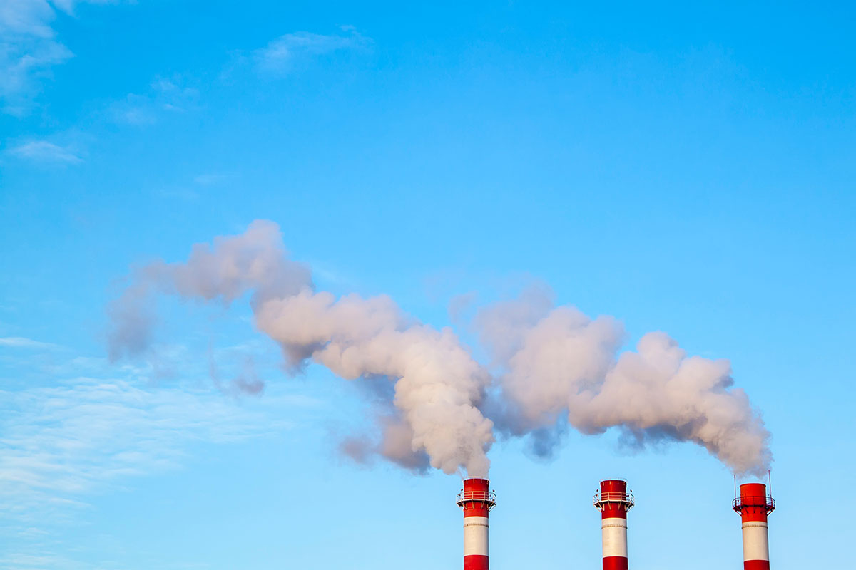 Three red and white industrial chimneys releasing white smoke plumes into a clear blue sky