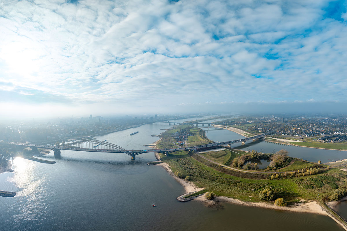 Aerial view of a river floodplain project with a second channel and arched road bridges beside a city
