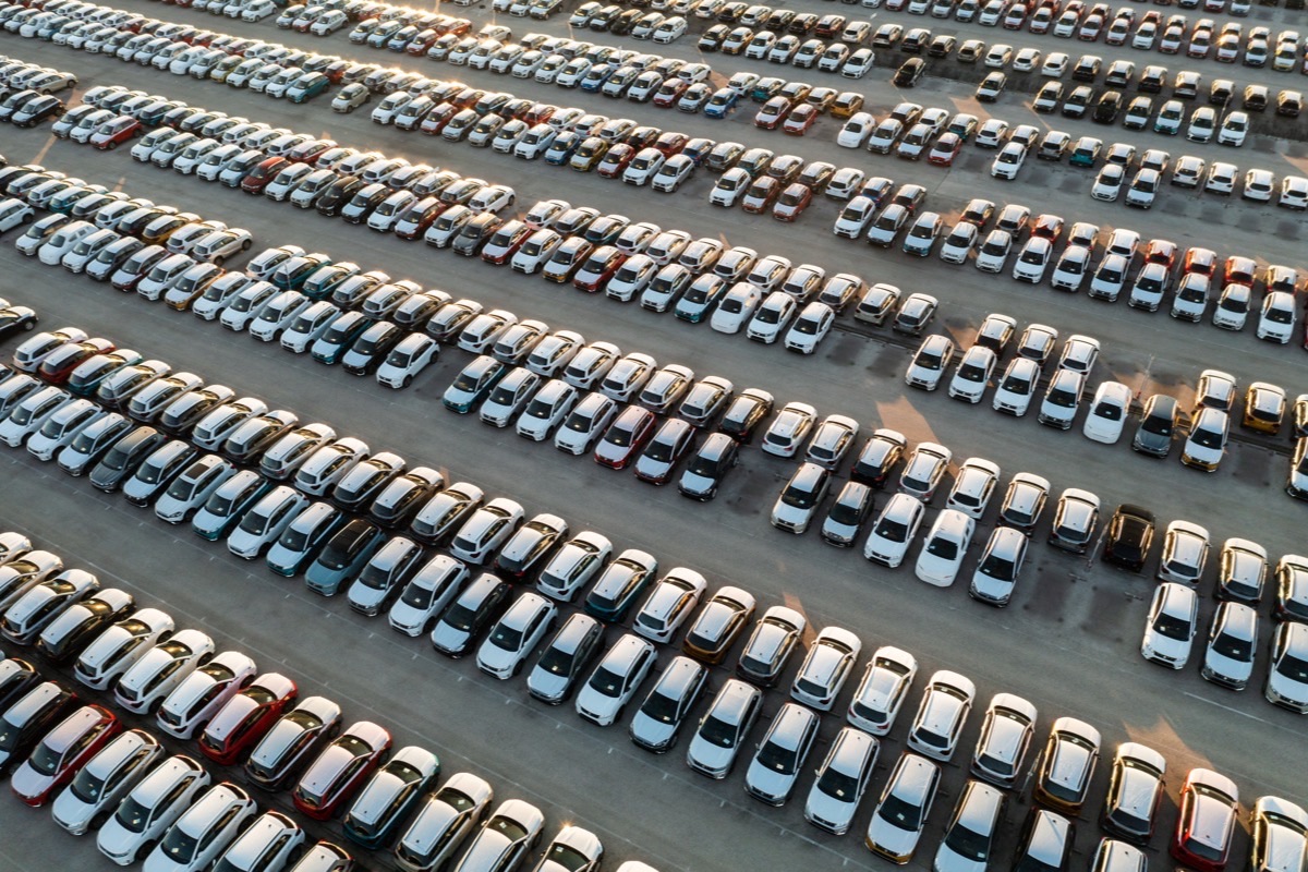 Aerial view of long rows of new cars parked at a vehicle distribution lot in late afternoon sun