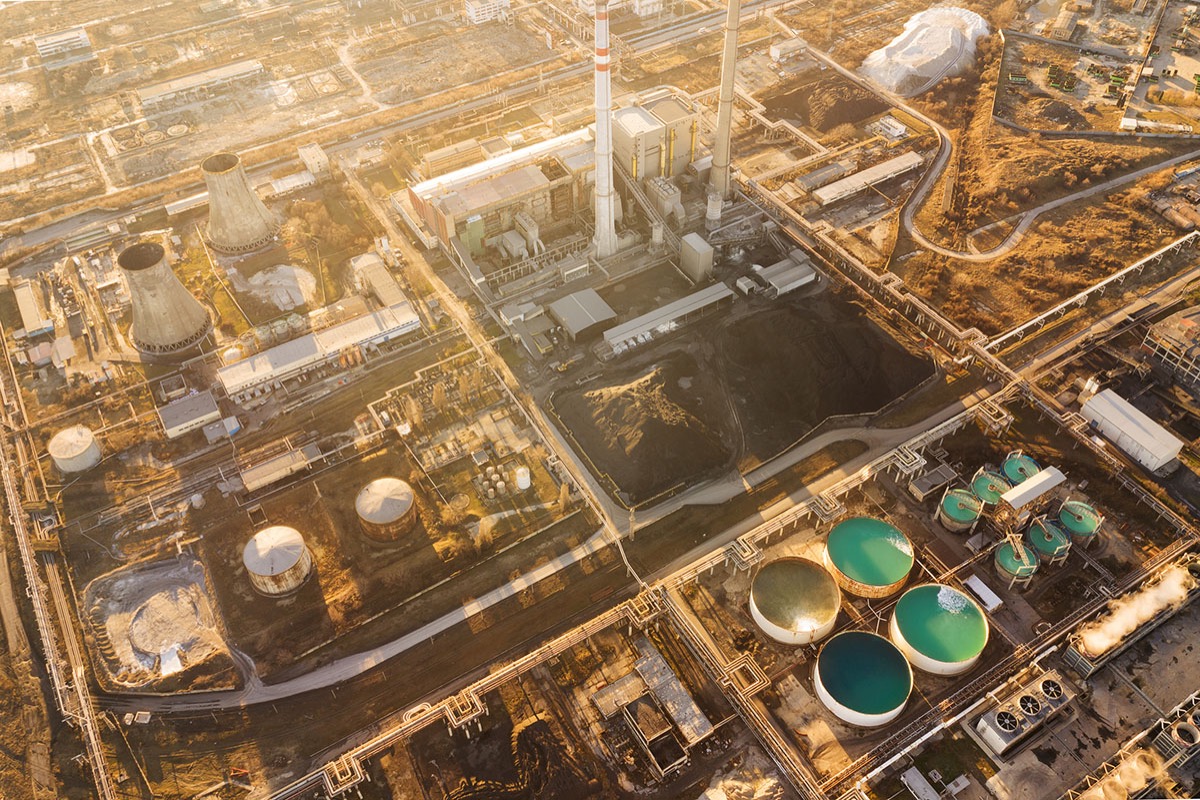 Aerial view of an industrial complex at sunset with cooling towers, smokestacks, coal stockpiles and storage tanks